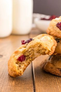 three cranberry white chocolate chip cookies on a wooden table next to a glass of milk