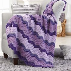 a purple blanket sitting on top of a couch next to a white chair in a living room