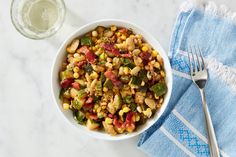 a white bowl filled with corn and vegetables next to a glass of water