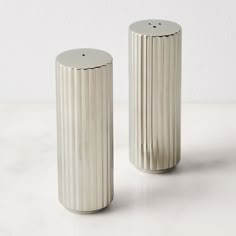 two silver vases sitting on top of a white countertop next to each other