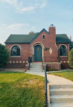 a red brick house with green grass and steps leading up to the front door on a sunny day