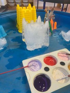 an artist's palette with paints and brushes on a blue table in front of ice sculptures