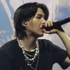 a woman with black hair holding a microphone up to her mouth and wearing pearls on it