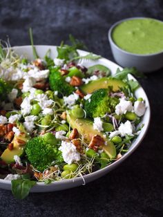 a salad with broccoli, cucumbers and other vegetables in a white bowl