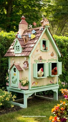 a bird house with two chickens in the window and flowers around it, sitting on top of a green lawn