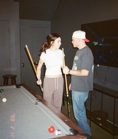 a man standing next to a woman near a pool table with a cue in it