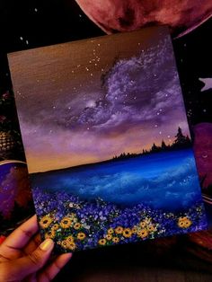 a person holding up a piece of art with flowers in front of the ocean and stars above it