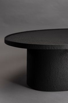 a black round table on a grey background with the top slightly turned to look like it is made out of concrete