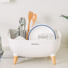 a white dish with utensils in it on a counter next to a plant