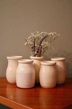 three white vases sitting on top of a wooden table next to a flower pot