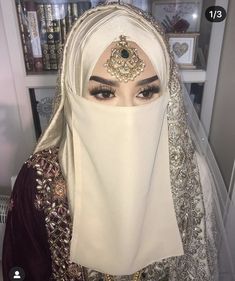 a woman wearing a white veil and headpiece with jewels on her forehead, in front of a bookshelf