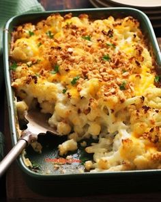 a green casserole dish filled with macaroni and cheese on a wooden table