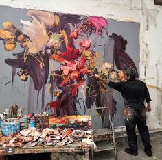 a man standing in front of a painting on a easel next to a table