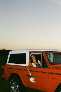 a woman sitting in the driver's seat of an orange and white pickup truck