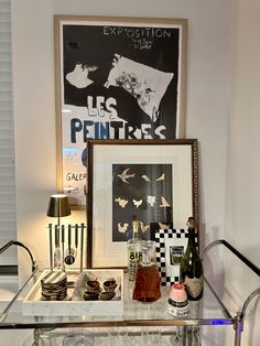 a glass table topped with lots of bottles and glasses next to a framed art piece