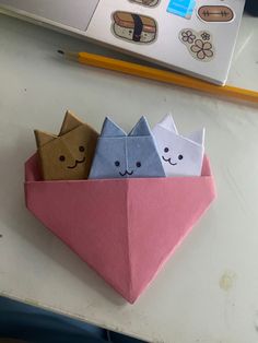 two origami cats in a paper boat on a table next to a pencil