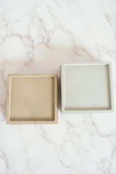 two square trays sitting on top of a white marble counter next to each other