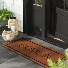 a door mat that says, come in and sits on the front porch next to potted plants