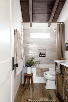 a white toilet sitting next to a bath tub in a bathroom on top of a wooden floor