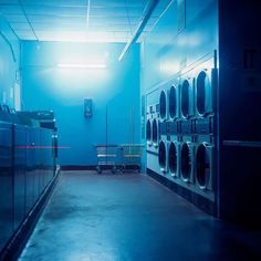 an empty laundry room with washers and dryer machines in the foreground, blue hues on the walls