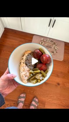 a person holding a bowl filled with food on top of a wooden floor next to a door