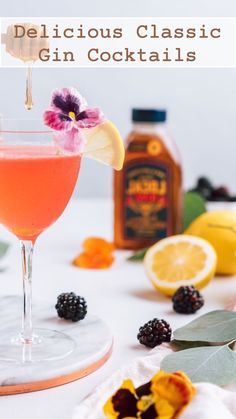 a glass filled with a pink cocktail next to lemons and blackberries on a white table