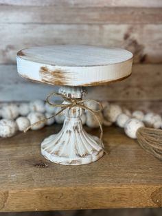 an old white cake stand on top of a wooden table next to beads and wood planks