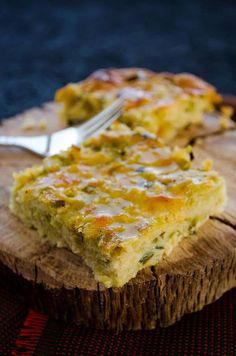 a slice of quiche sitting on top of a wooden cutting board next to a fork