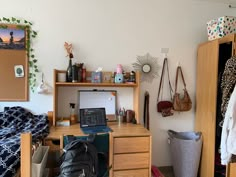 a desk with a laptop on it in a room filled with clothes and other items