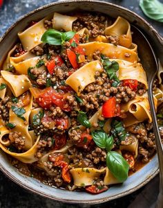 a bowl filled with pasta and meat on top of a table next to a fork