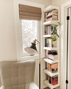 a white chair sitting next to a window in a room with bookshelves and a lamp