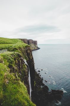 a waterfall is coming out of the side of a cliff into the ocean on a cloudy day