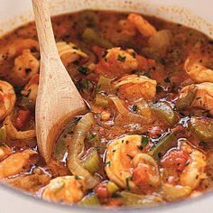 a wooden spoon in a bowl filled with shrimp and vegetable stew on top of a table