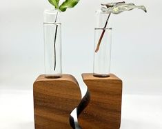 two vases with flowers in them sitting on wooden bases, one is empty and the other has water inside