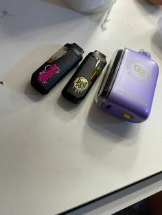 three cell phones sitting next to each other on a white counter top in front of a cup