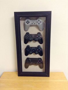 three video game controllers are in a shadow box on a wooden table next to a white wall