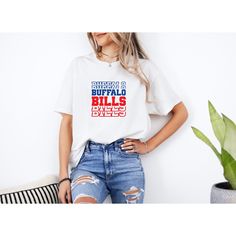 a woman wearing a buffalo bills t - shirt with ripped jeans and a plant in the corner