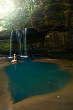 a woman is sitting in the middle of a pool with a waterfall behind her,