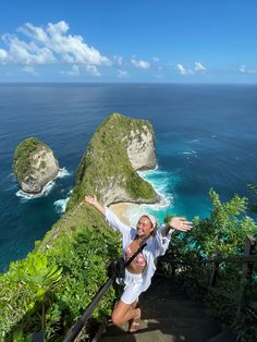 a woman standing on top of a set of stairs next to the ocean with her arms outstretched