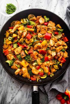 a skillet filled with chicken and veggies on top of a marble counter