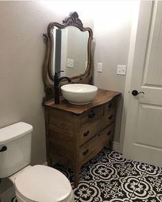 a white toilet sitting next to a wooden dresser under a mirror on top of a sink