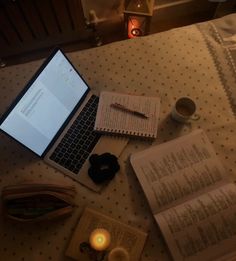 a laptop computer sitting on top of a bed next to an open book and candle