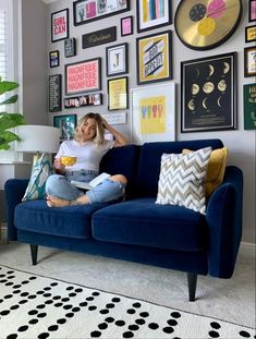 a woman sitting on top of a blue couch in front of a wall full of pictures