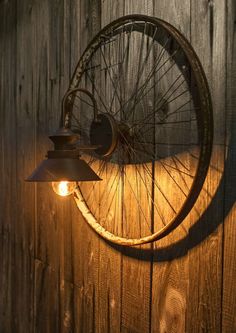 an old bicycle wheel mounted to the side of a wooden wall next to a lamp