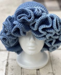 a white mannequin head wearing a blue crocheted hat with large ruffles