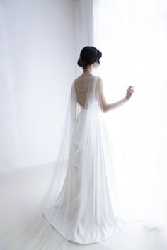 a woman in a wedding dress looking out the window with her veil draped over her head