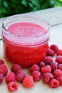 raspberry sauce in a glass jar with fresh raspberries around it on a wooden table