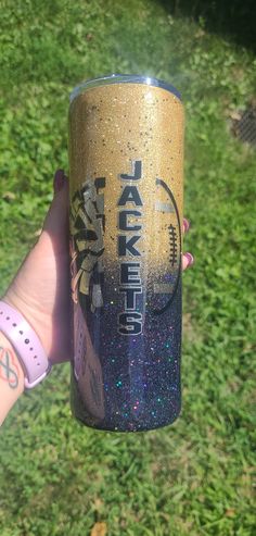 a person holding up a cup with glitter on it in front of some green grass