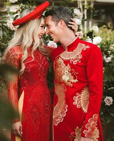 a man and woman dressed in red standing next to each other with flowers behind them