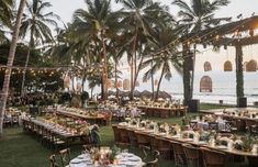 an outdoor dining area with palm trees and tables set up on the grass near the ocean